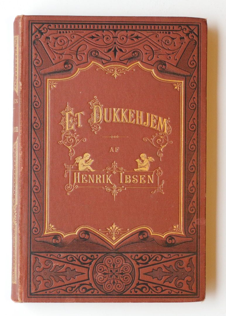 Red cloth-bound book cover with gold ornamental border and the title 'Et Dukkehjem' by Henrik Ibsen in gold lettering, vintage Victorian style.